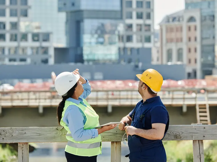 Dois profissionais de capacete conversando em frente a edifícios